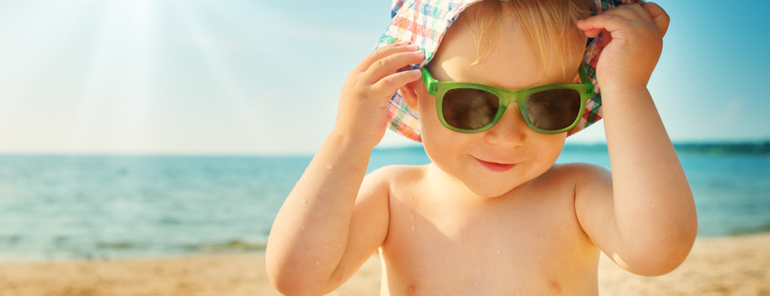 one year old boy smiling at the beach in hat with sunglasses. Child on vacations at sea