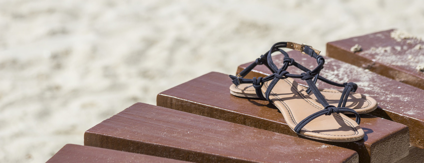 female brown sandals on a wooden table on the beach background. Concept of a summer rest and travel