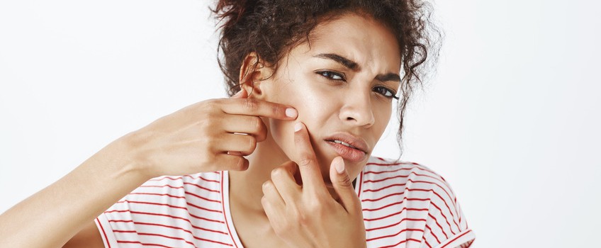 Close-up shot of intense upset woman bending towards camera and squeezing acne with index fingers on cheek, frowning, trying to get out pimple, being sad with bad facial condition right before date.
