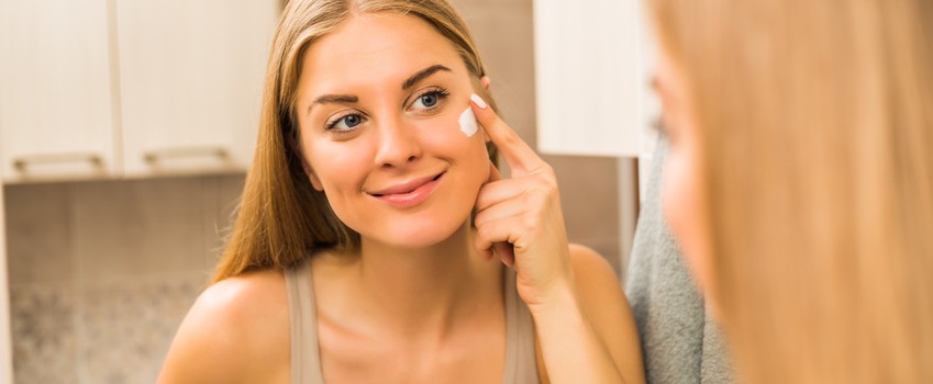 Beautiful woman applying moisturizer on her face.